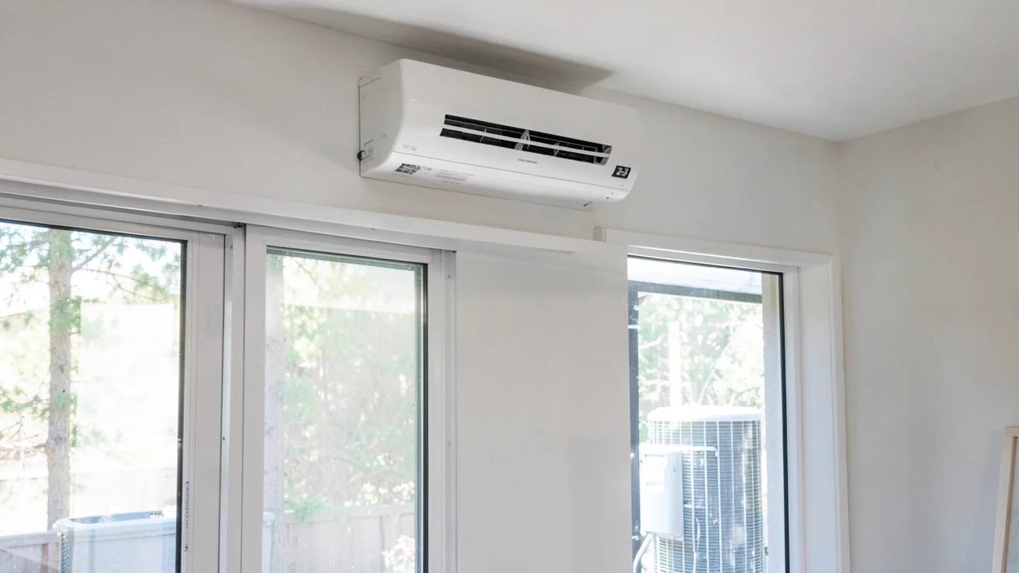 A wall mounted ductless mini split unit above a window with an outdoor condenser visible outside