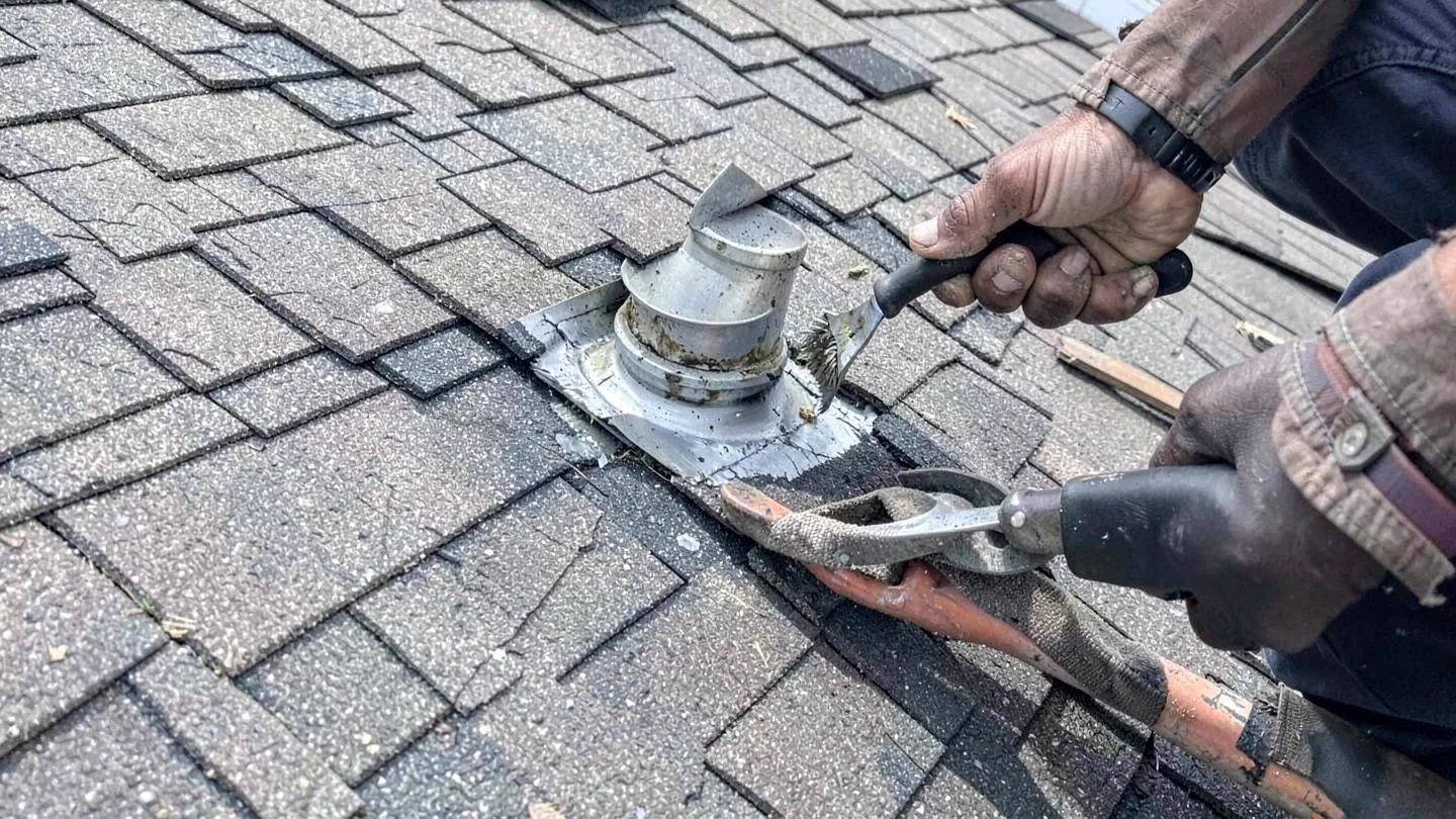 A roofer resealing flashing around a vent pipe while patching a small roof section