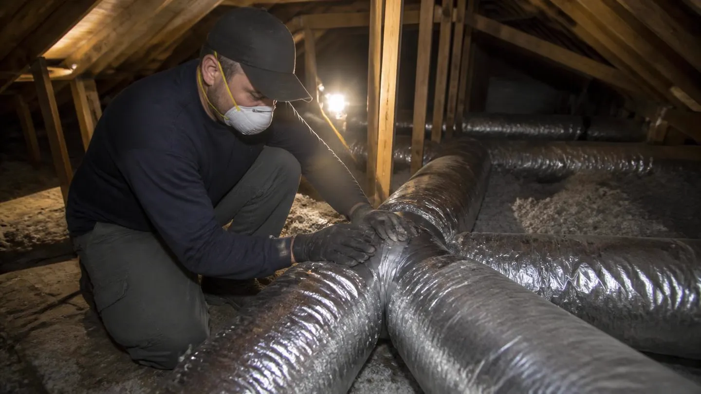 A technician sealing a flexible duct connection in a residential attic