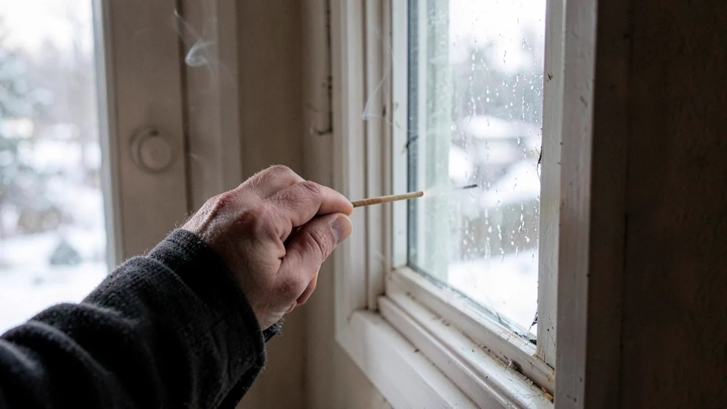 A homeowner tracing a draft along an old window sash on a snowy day